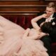 happy couple lounging on a red velvet couch. The bride wears a blush wedding dress and the groom has a tuxedo with a pink tie