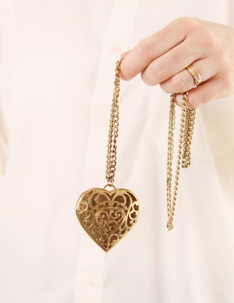 a gold heart-shaped locket held by a woman with a wedding ring