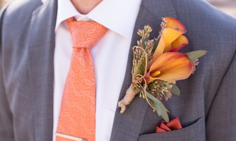 groom wearing a large orange flower as his boutonniere
