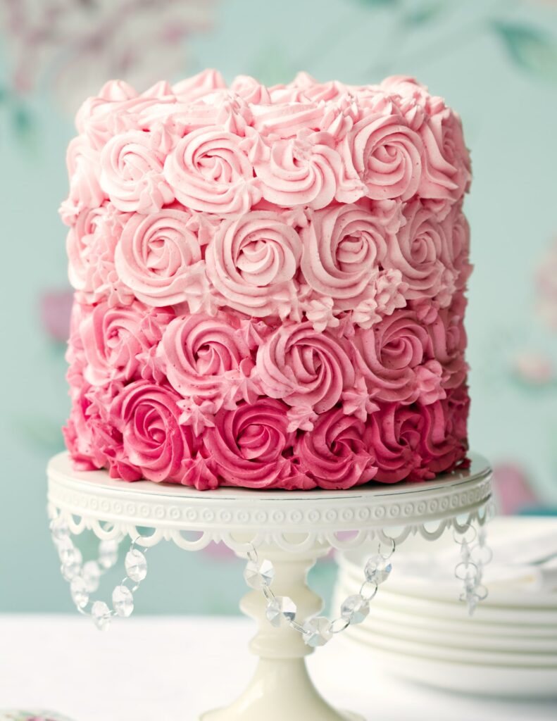 wedding cake with different shades of pink frosting on a cake stand
