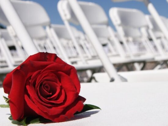 a single red rose laid on a white folding chair at a wedding ceremony
