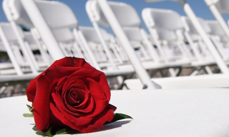 a single red rose laid on a white folding chair at a wedding ceremony