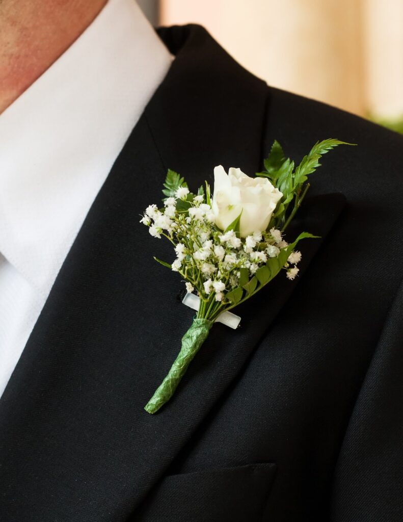 simple, classic boutonniere pinned to a groom's jacket with a white flower