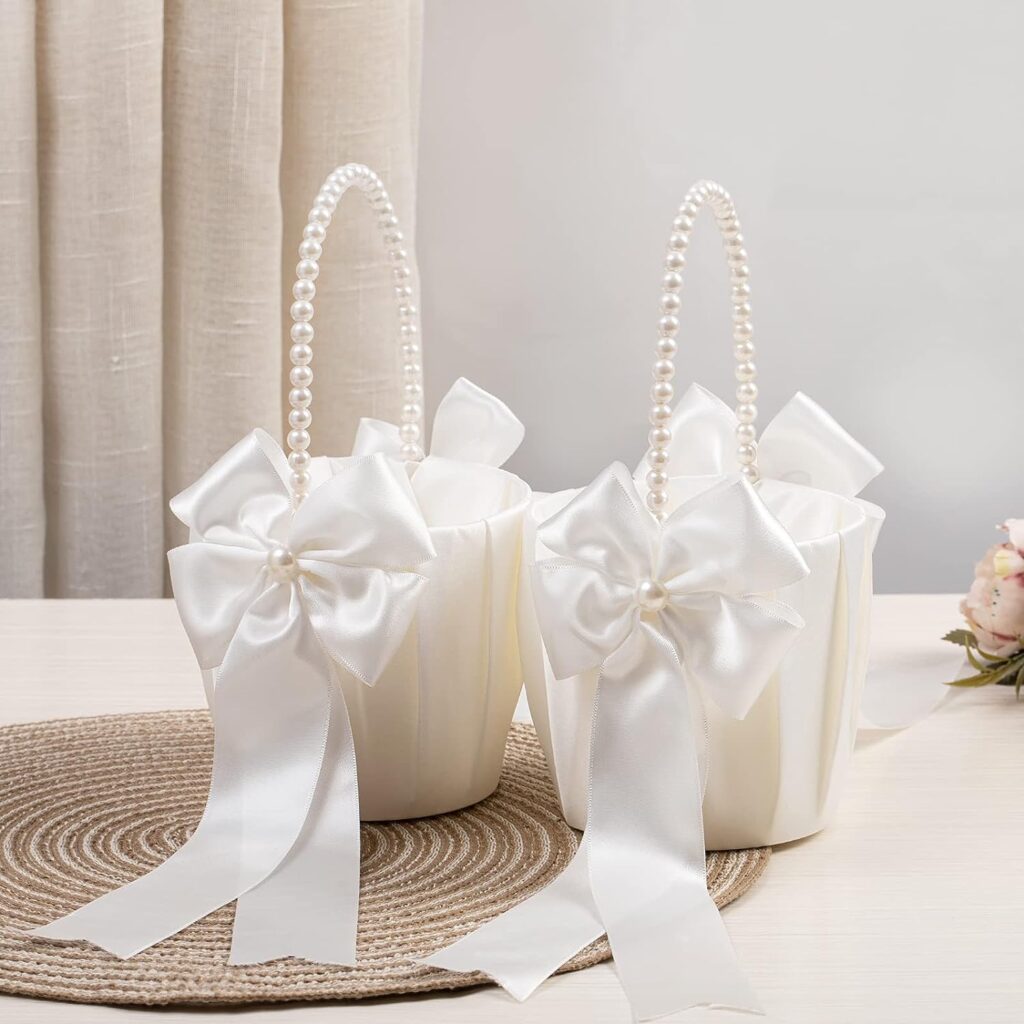 Two satin flower girl baskets with pearl handles. They have a large white bow tied to the handles.