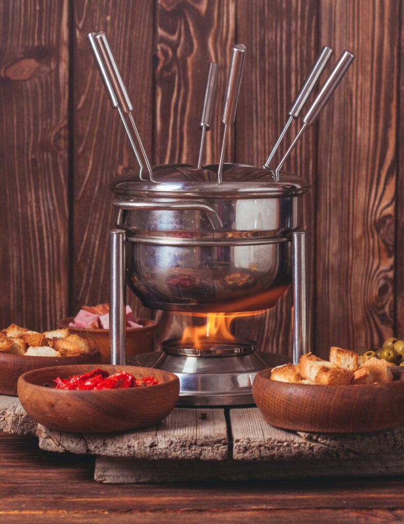 a fondue station with bowls of bread, meats, olives, and peppers
