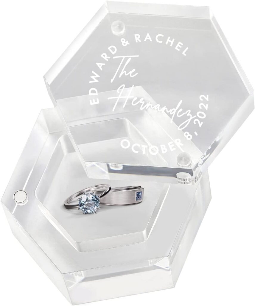Glass, hexagonal wedding ring holder. On the lid are the bride and groom's name and wedding date. Inside is a silver set of wedding bands with crystal blue stones.