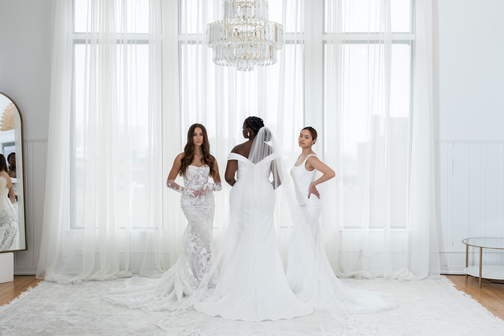 three women in different bridal gowns in white room