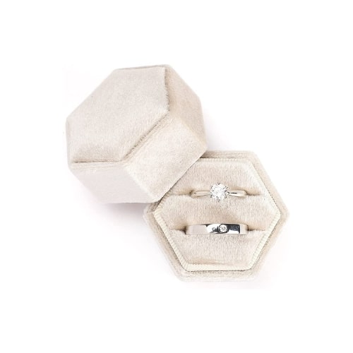 Hexagonal, ivory suede ring box. The lid of the box is leaning up against the base of the box and inside are a set of silver wedding rings.