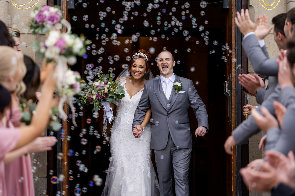 bride and groom leaving their wedding through a shower of bubbles blown by their guests