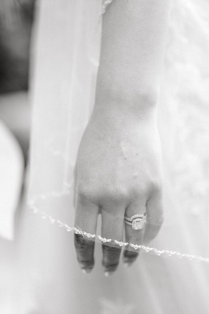 Close up of a bride's left hand and her stunning ring. She is wearing her wedding dress and the veil is hanging over her fingers.