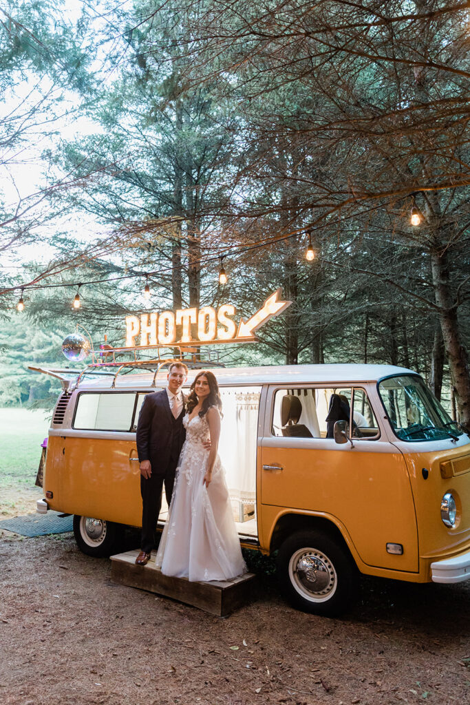 Bride and Groom standing in front of an antique Volkswagon bus in the woods.