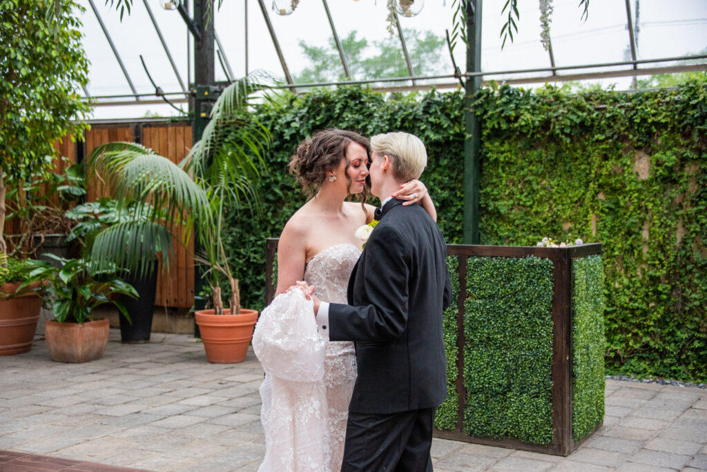 Corinne and Alicia at the Planterra Conservatory, wearing the Allure dress and the Randazzo Formalwear suit. They are about to share a kiss.