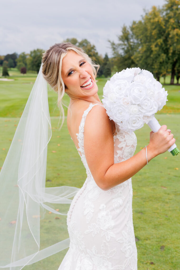 bride outside on her wedding day wearing a dress and veil and holding a white bouquet