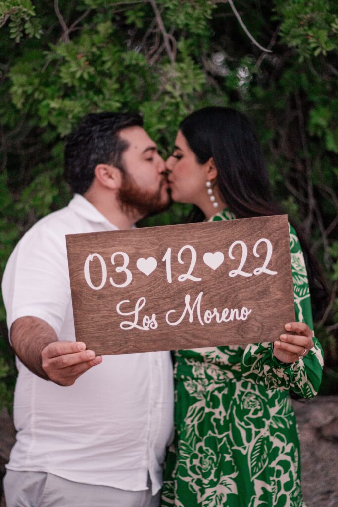 bride- and groom-to-be sharing a kiss while showing their save the date sign