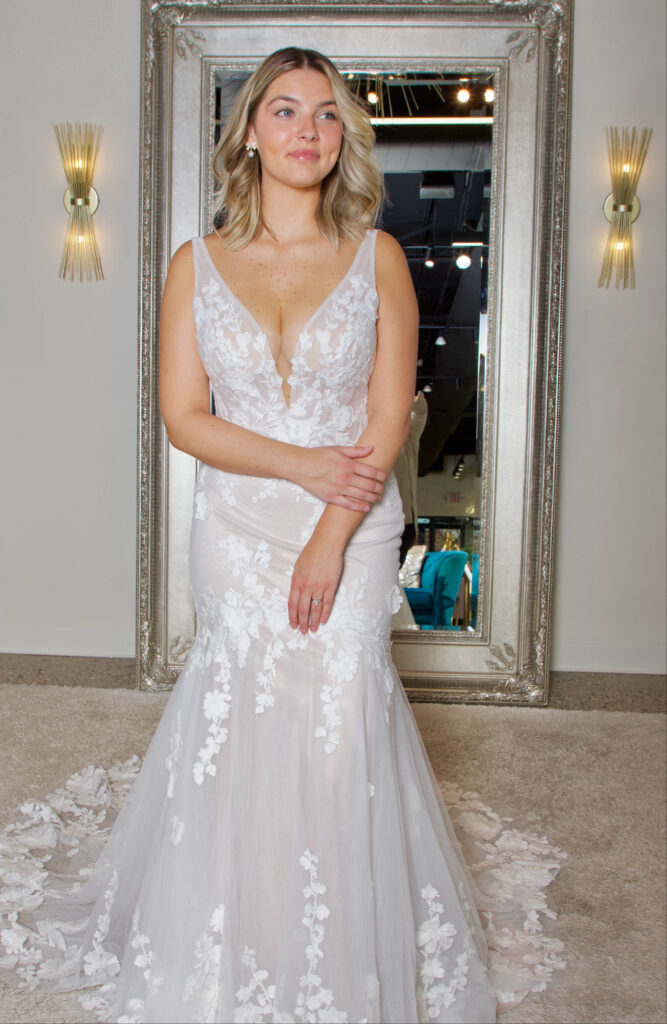 Holly is a vneck fit and flare gown with flattering ruched detail on the back and a natural leaf patterned lace. This gown has no sparkle and is romantic and elegant