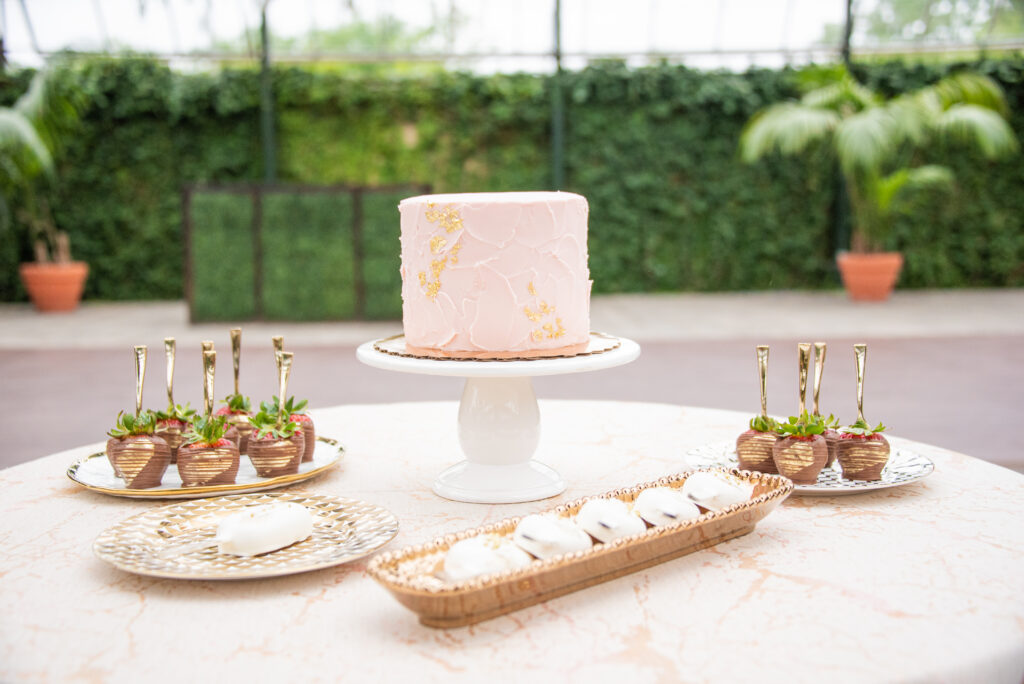 a small dessert table with a pink wedding cake and chocolate covered strawberries