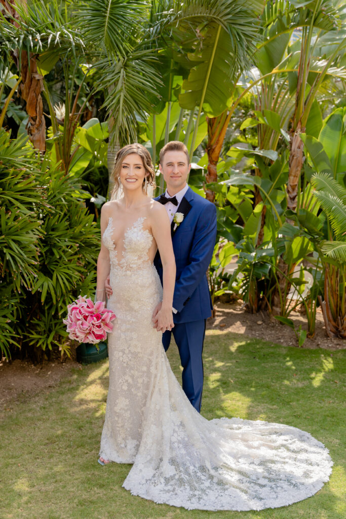 a bride and groom at a tropical destination for their wedding. The bride holds an exotic pink floral bouquet