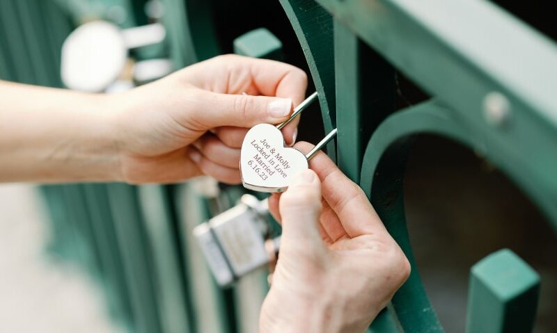 woman locking a heart-shaped lock onto a bridge to signify everlasting love