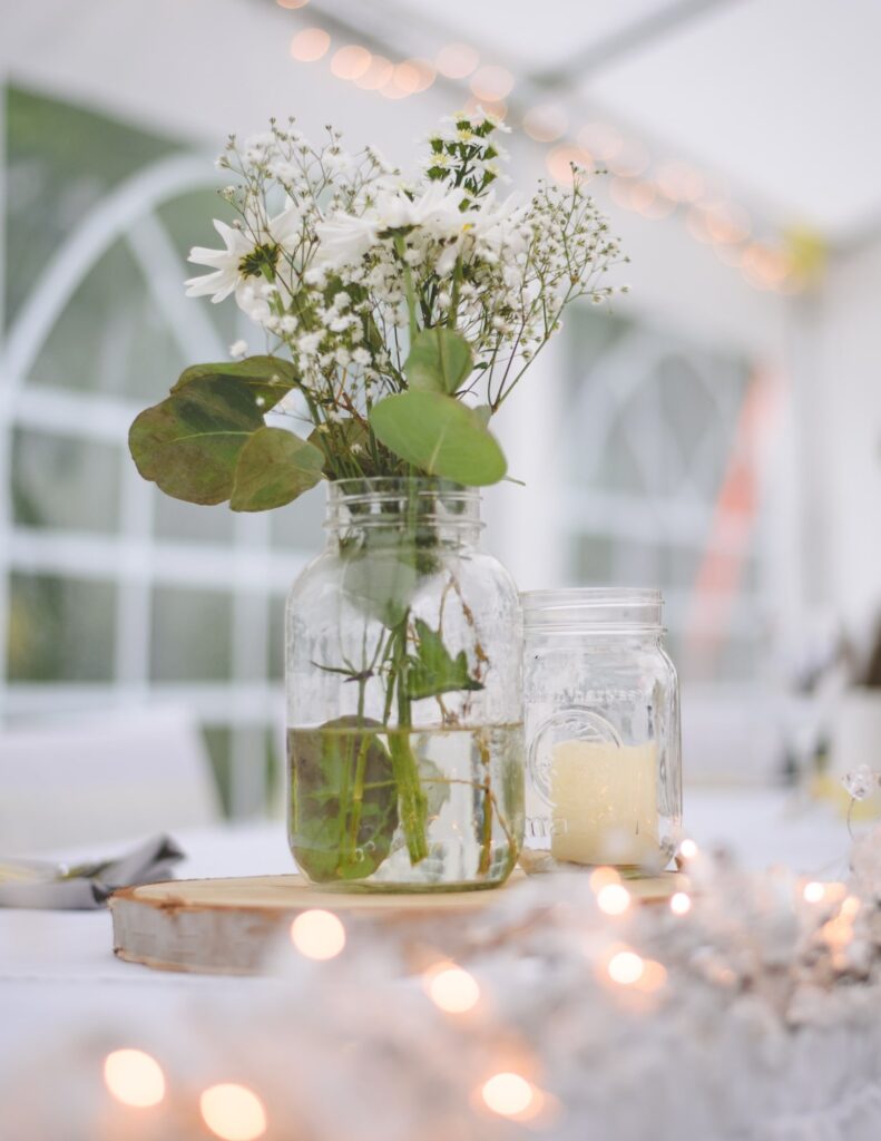 a table setting with two glass mason jars with a candle and flowers in them