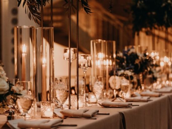a warmly lit wedding table with greenery hanging above and several candles alight on the table