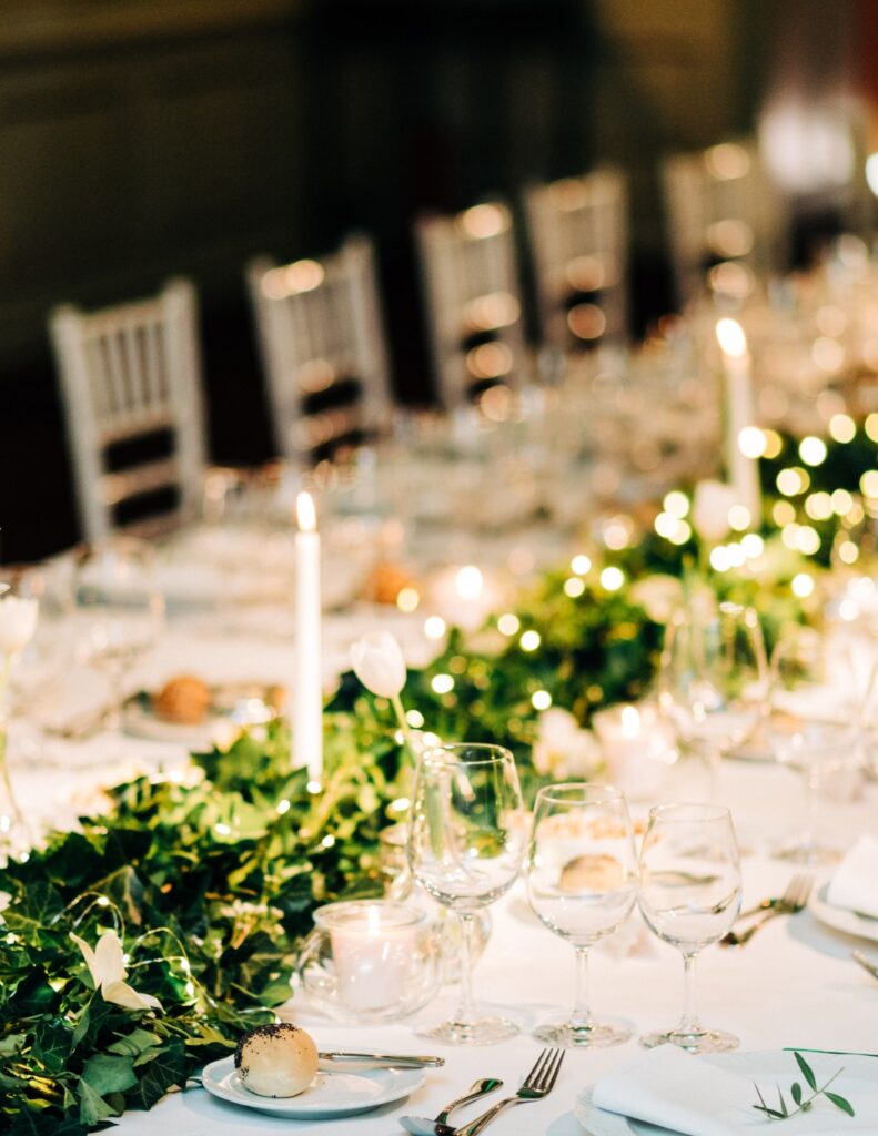a white wedding table set up with greenery in the center and candles