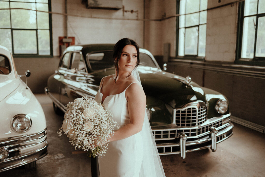 bride holding her bouquet in front of retro automobiles at the Packard Proving Grounds venue
