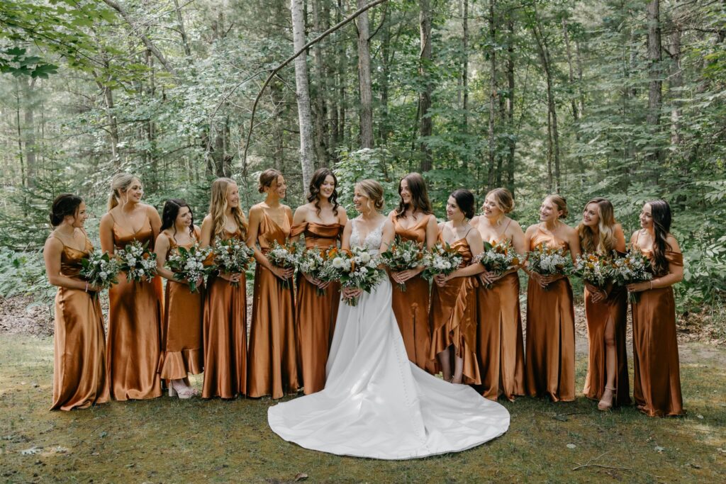 bride and her bridesmaids holding summer flowers in front of a forest