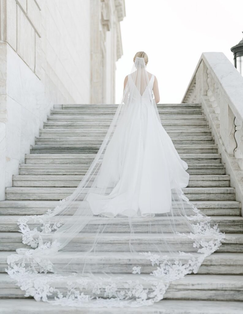 a bride standing on a set of marble stairs with her long train flowing behind her, posed for a wedding photo