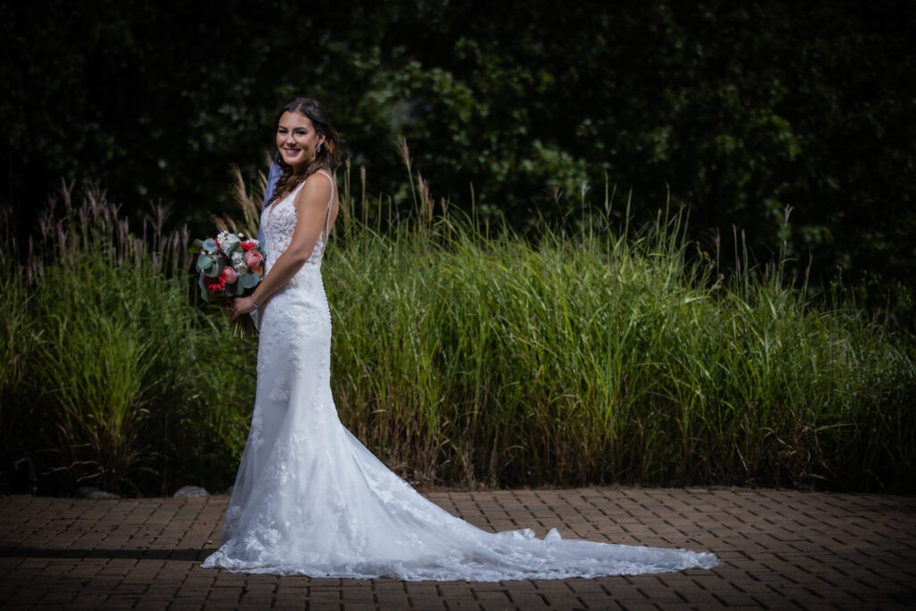 a bride in front of a forest holding a bouquet of red, white, and pink flowers