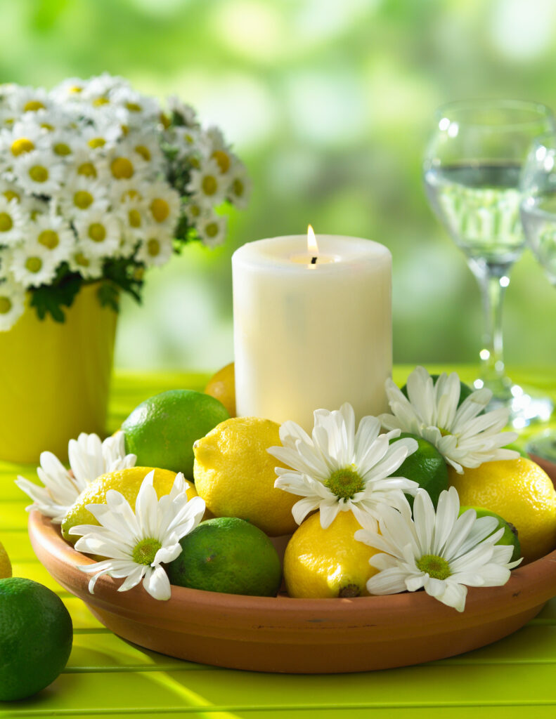 a white candle surrounded by lemons, limes, and daisies