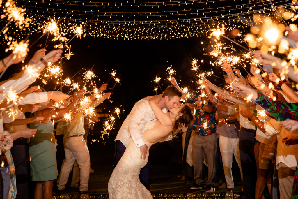 a newly married couple sharing a romantic kiss surrounded by wedding guests holding sparklers