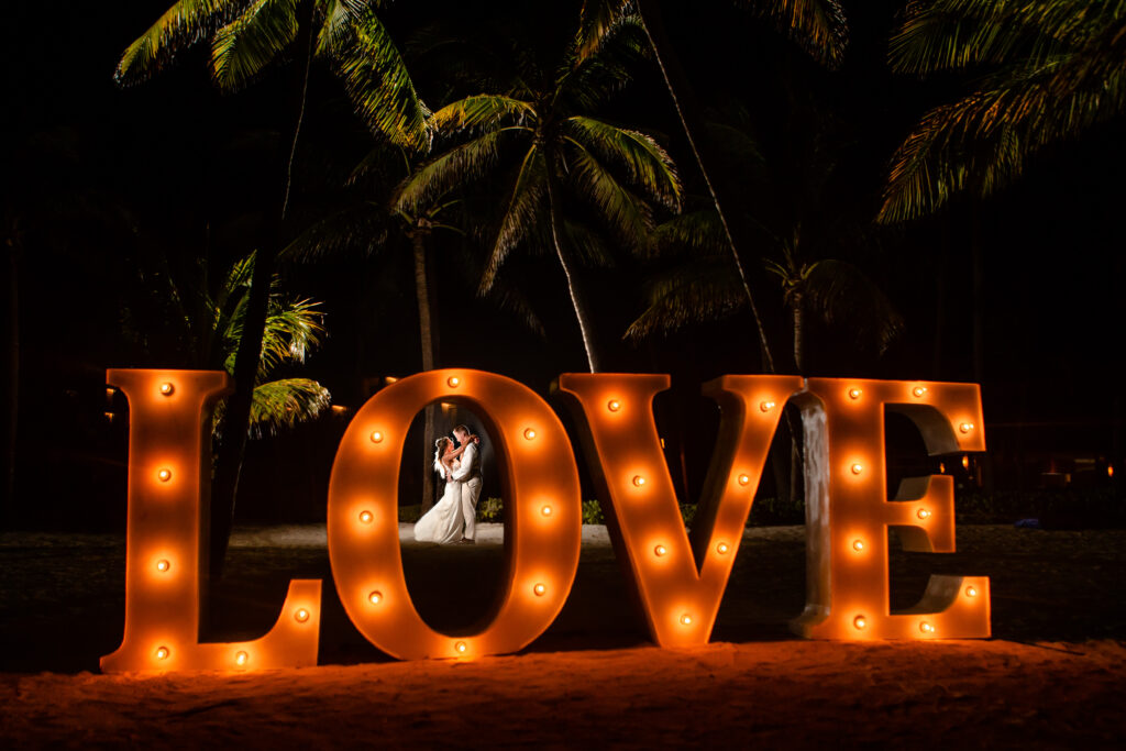 a couple holding each other behind a giant sign that says LOVE in a tropical setting