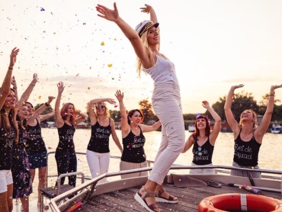 a woman wearing a captain's hat on the bow of a ship surrounded by her bachelorette party
