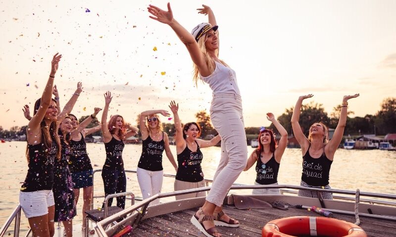 a woman wearing a captain's hat on the bow of a ship surrounded by her bachelorette party