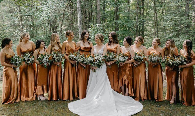bride and her bridesmaids holding summer flowers in front of a forest