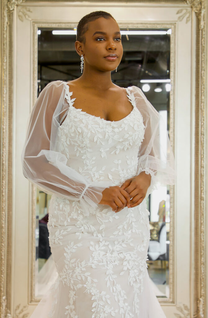 Emery is a trumpet styled scoop neckline with leafy applique and removable bishop sleeves.