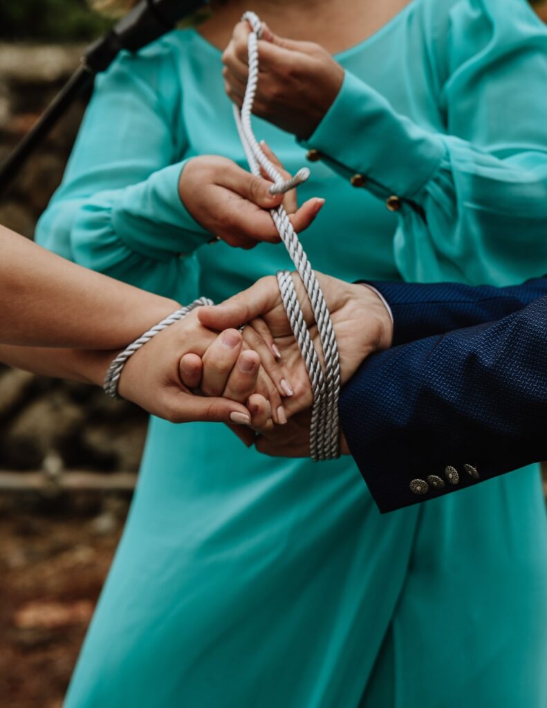 a woman tying a couple's hands together in a traditional wedding handfasting ceremony
