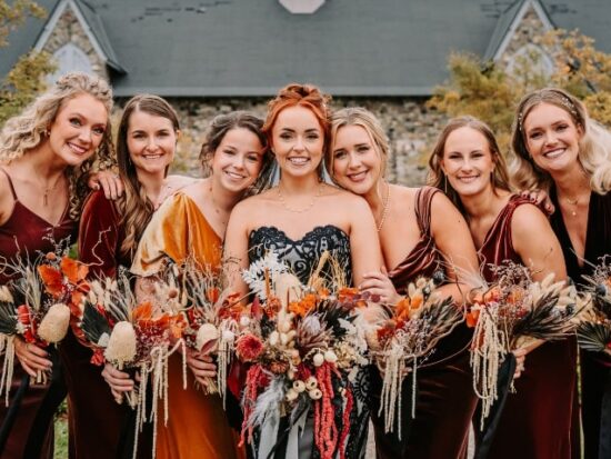 bride and bridesmaids smiling and holding striking bouquets of autumnal flowers and fall-themed dresses
