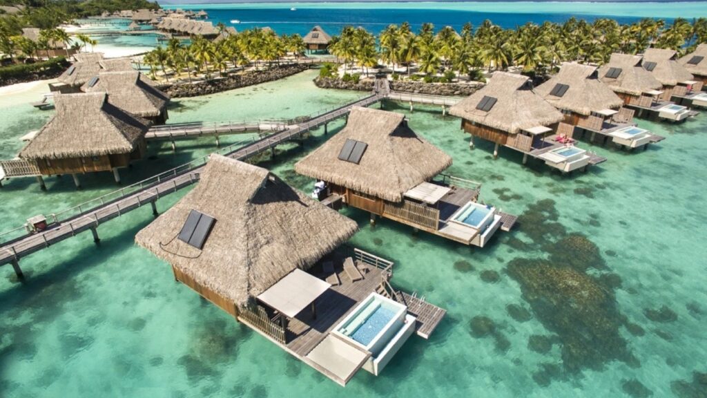 A stunning helicopter shot of houses on the water in Bora Bora with tropical palm trees in the background.