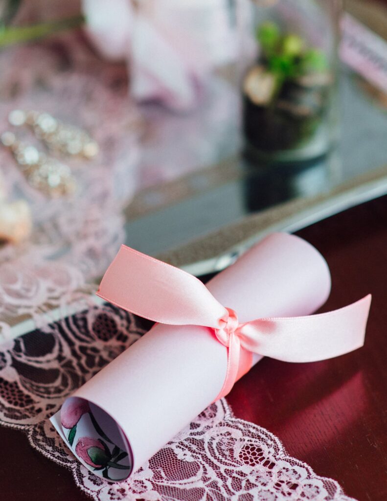 a pink wedding invitation on a bit of lace tied with a pink ribbon