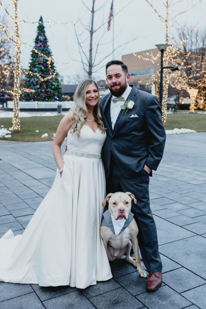 Newly married husband and wife stand with their dog outside their wedding venue