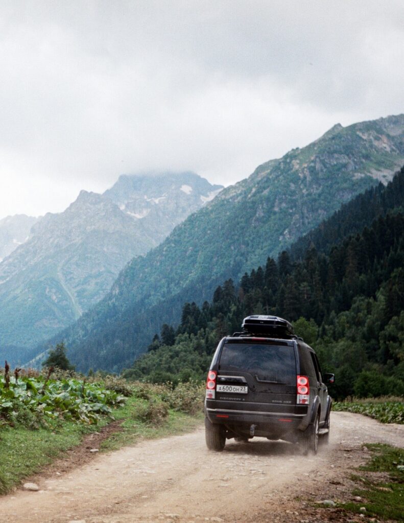 A black SUV driving on a dirt trail through a mountainous area on a cross-country road trip