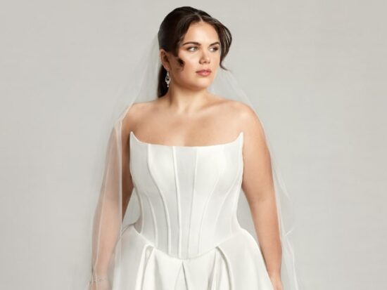 A woman wearing Caroline, an elegant basque waistline wedding dress with a modified scoop neckline