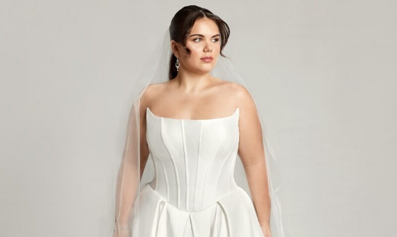 A woman wearing Caroline, an elegant basque waistline wedding dress with a modified scoop neckline