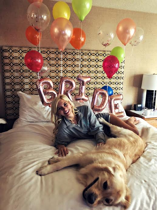 A bride lounging on a bed on the morning of her wedding with her golden retriever