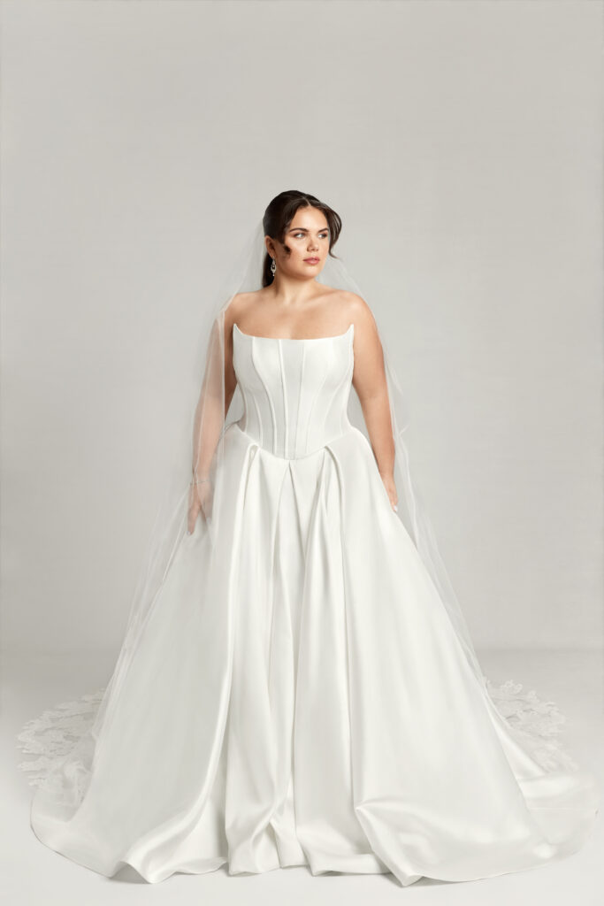 A woman wearing Caroline, an elegant basque waistline wedding dress with a modified scoop neckline