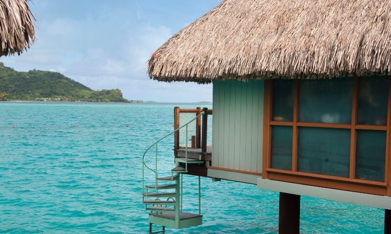 a tropical island in the background and a bungalow suspended over the ocean in the foreground