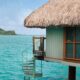 a tropical island in the background and a bungalow suspended over the ocean in the foreground