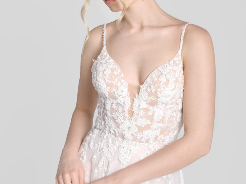 Shy bride wearing a spaghetti strap wedding dress with a deep v cut neckline and floral detailing on the bodice that flows down onto the flowy, tulle skirt.