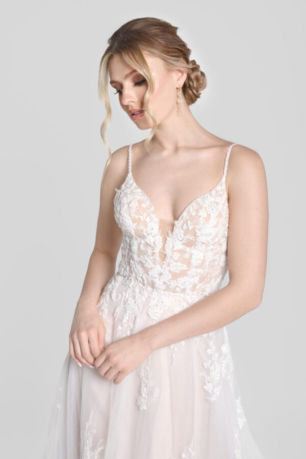 Shy bride wearing a spaghetti strap wedding dress with a deep v cut neckline and floral detailing on the bodice that flows down onto the flowy, tulle skirt.